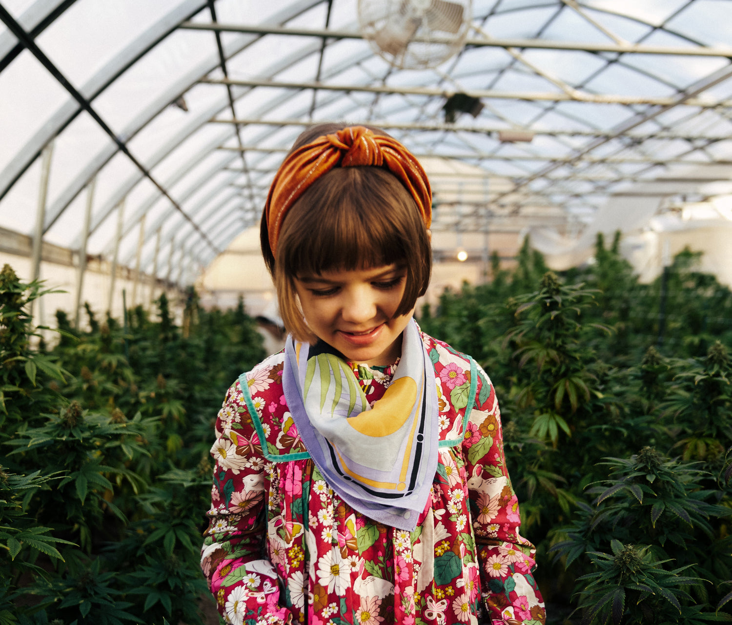 Person wearing a colorful floral jacket and headband in a greenhouse setting