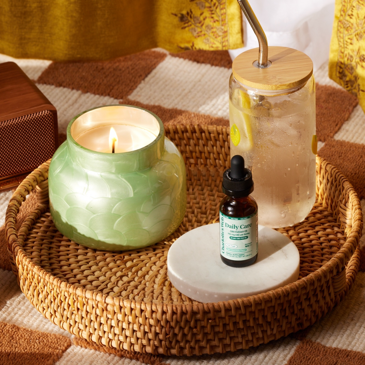 Candle, bottle, and glass on a woven tray with a checkered tablecloth