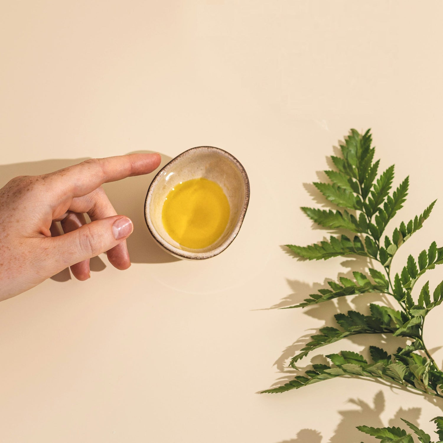 Hand reaching to oil container with herbs laid on beige background