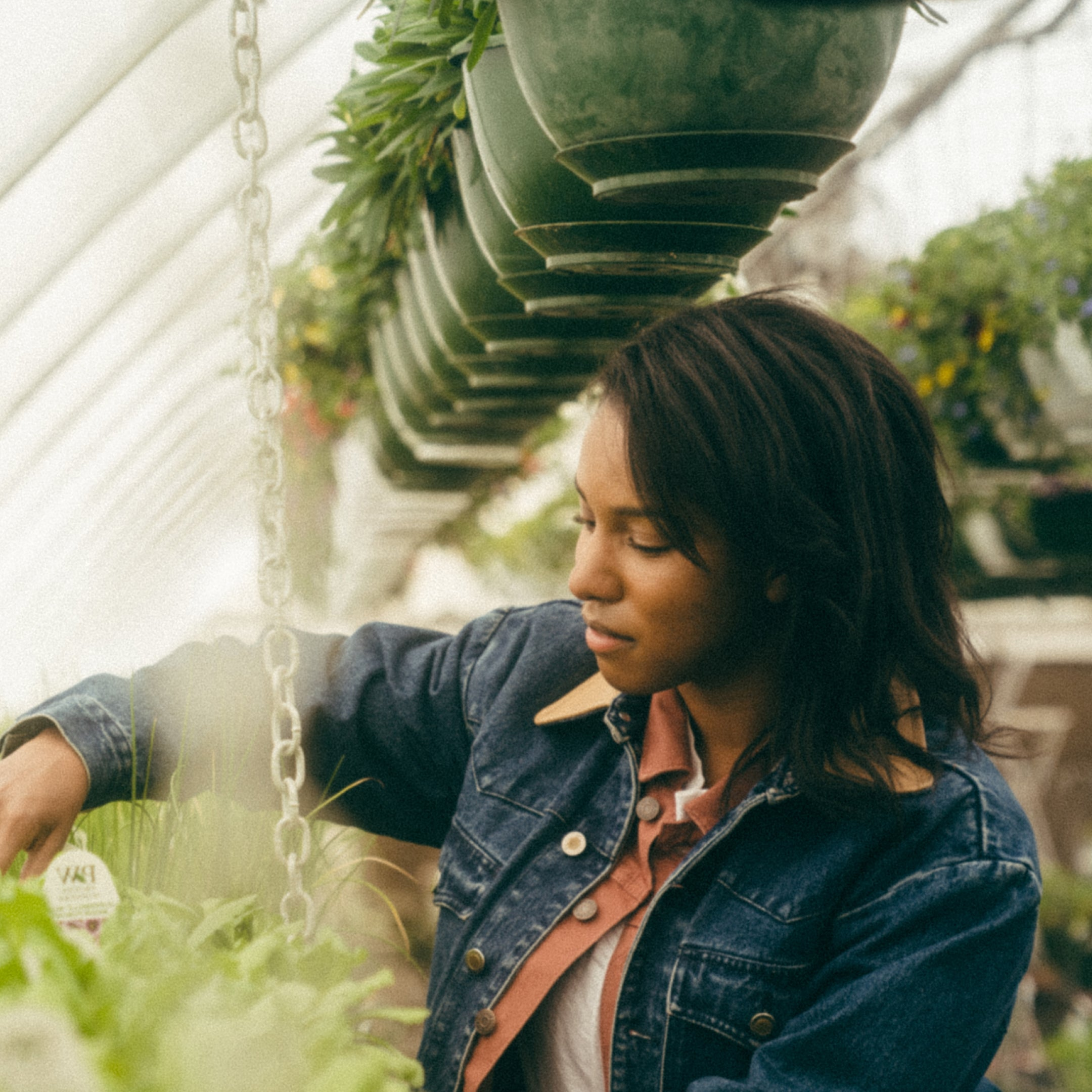 Woman in a denim jacket standing in a greenhouse with plants around her.