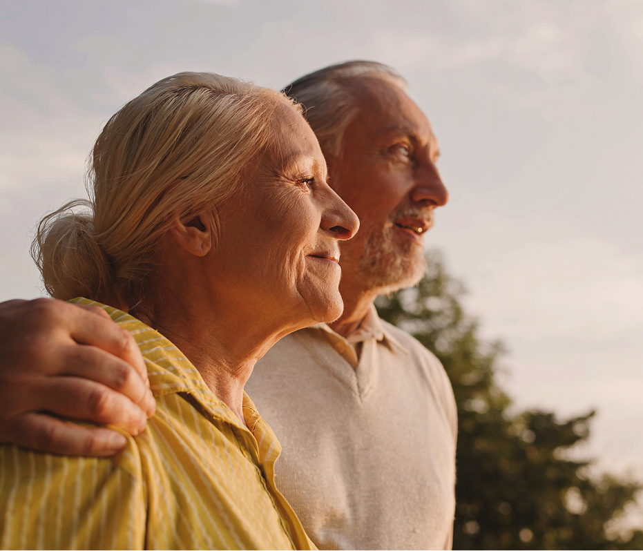 Two elderly people standing close together with a blurred natural background