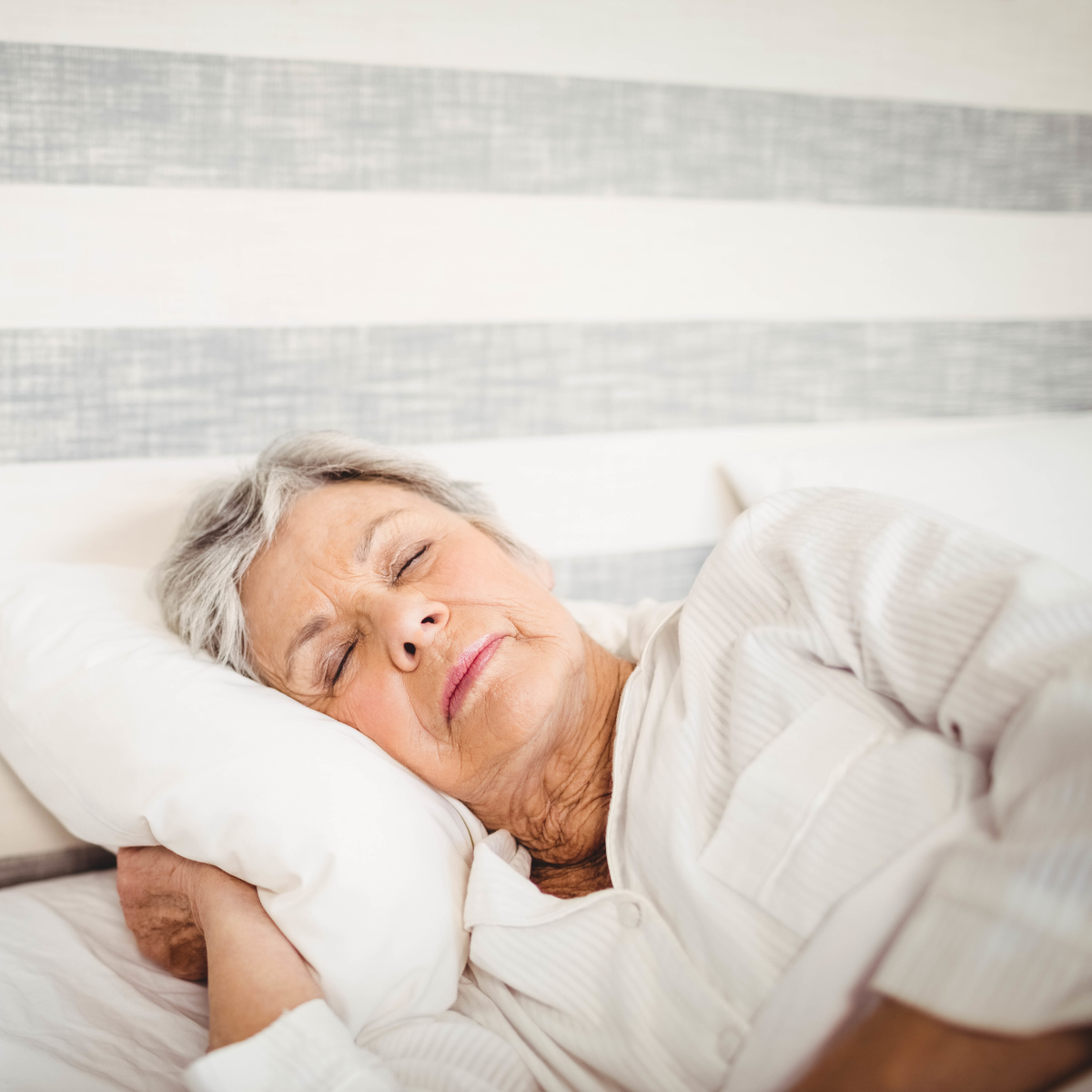 Senior woman sleeping peacefully in bed with white bedding.